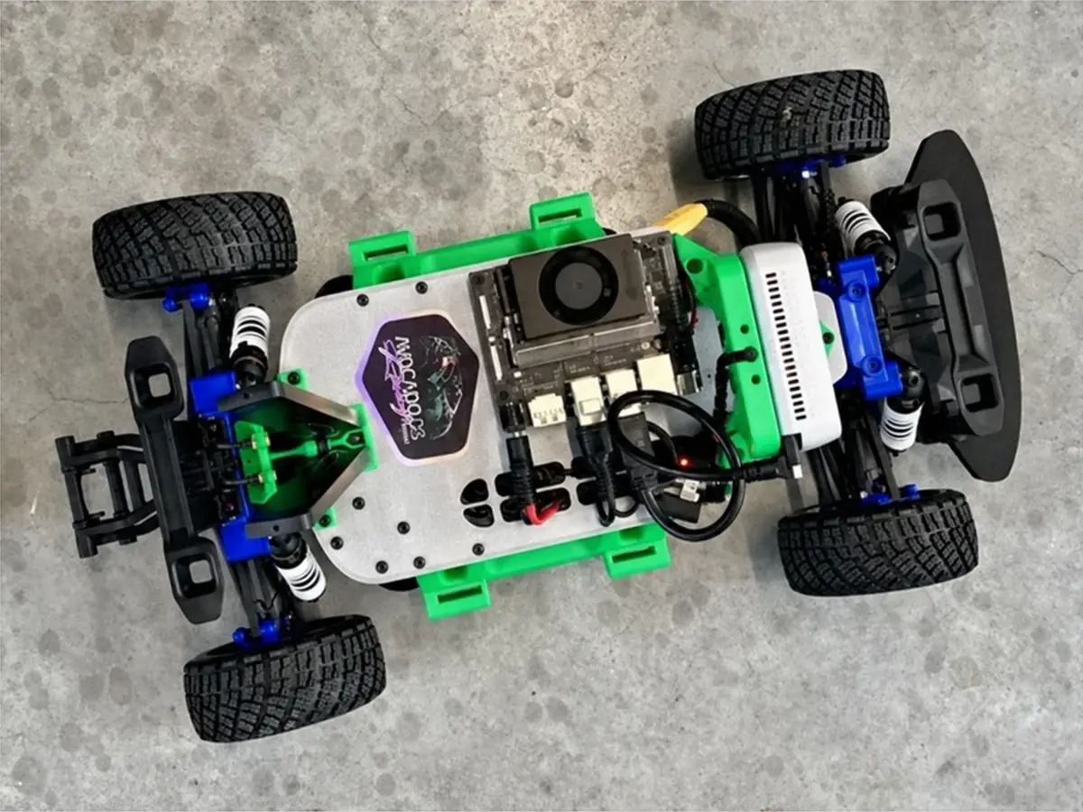 A GOAT Racer 3 car seen from above with its body off, showing the Jetson module, depth camera and an Avocado OS Racing Team sticker on its green and white chassis